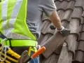 Pracownik w kamizelce odblaskowej usuwa eternit z dachu. Dowiedz się, ile kosztuje demontaż eternitu i jak bezpiecznie to zrobić.