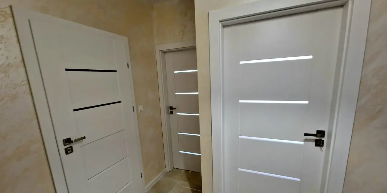 Nowoczesne drzwi Drea Auri w białym kolorze, z eleganckimi, poziomymi przeszkleniami, tworzą stylowe przejście w korytarzu.