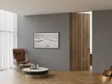 Nowoczesne wnętrze z betonową ścianą, fotelem, stolikiem kawowym i otwartymi drzwiami rewersyjnymi dre. Widoczne schody i obraz na ścianie.