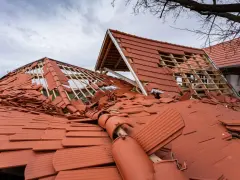 Uszkodzona ondulina na dachu, wiele dachówek jest połamanych i leży na ziemi.