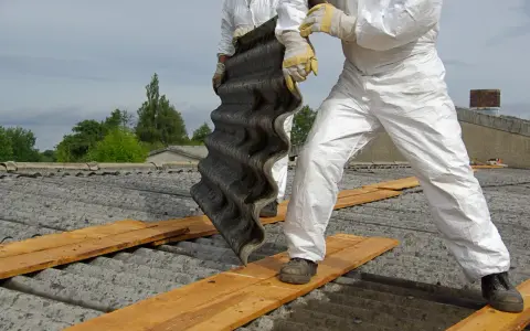 Osoby w kombinezonach ochronnych usuwają eternit z dachu. Koszt usunięcia azbestu zależy od wielu czynników.