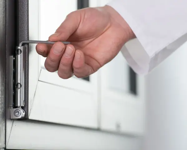 Dłoń reguluje zawias okna kluczem imbusowym, przygotowując je do zimy.