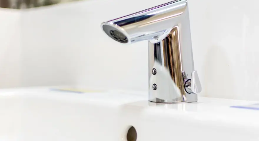 Elegancka bateria umywalkowa z korkiem, wykonana z chromowanego metalu, lśni na białej ceramice.