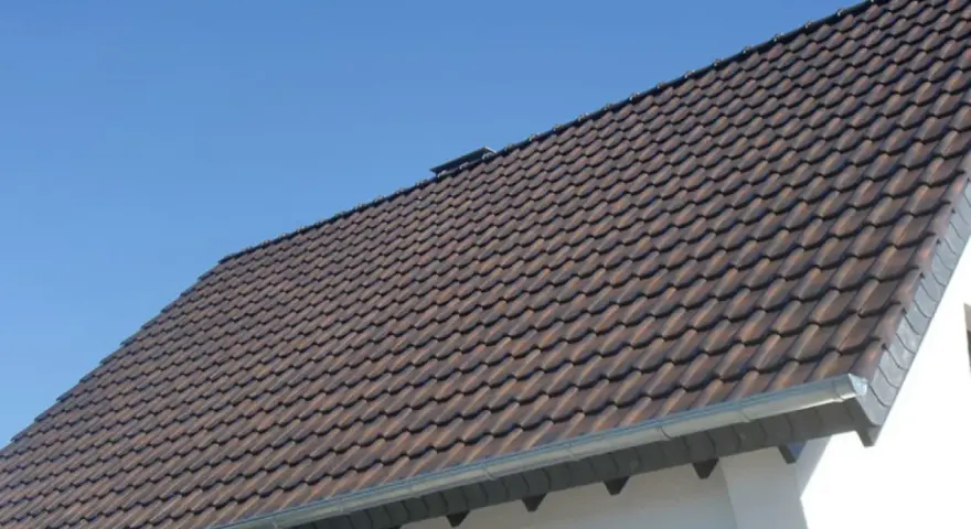 Dachówki ceramiczne na dachu domu, z widocznym okapem. Okap jest kluczowy, by wiedzieć, ile powinien wystawać dach poza ścianę, chroniąc ją przed deszczem.