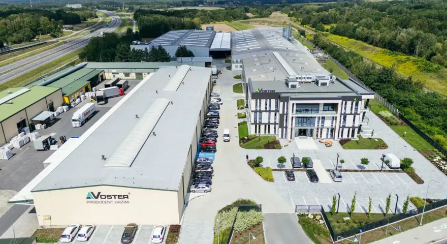 Nowoczesny kompleks produkcyjny Voster producent drzwi, z drogą szybkiego ruchu w tle.