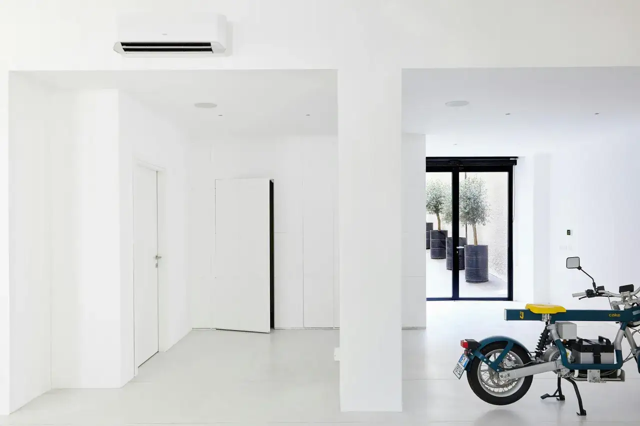 Minimalistyczne wnętrze z klimatyzatorem, białymi drzwiami bezprzylgowymi i nowoczesnym motocyklem.