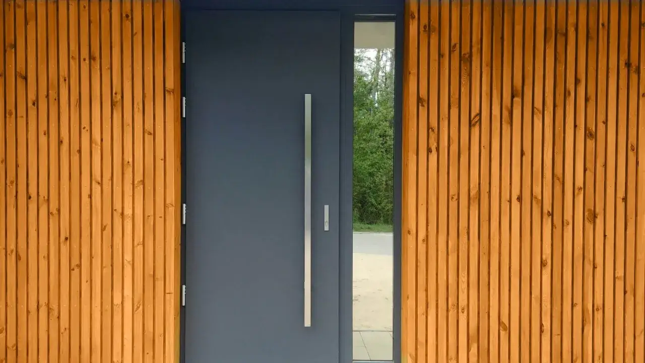 Nowoczesne, ciemnoszare drzwi wejściowe wygłuszające z długą, metalową klamką, otoczone pionowymi, drewnianymi deskami.