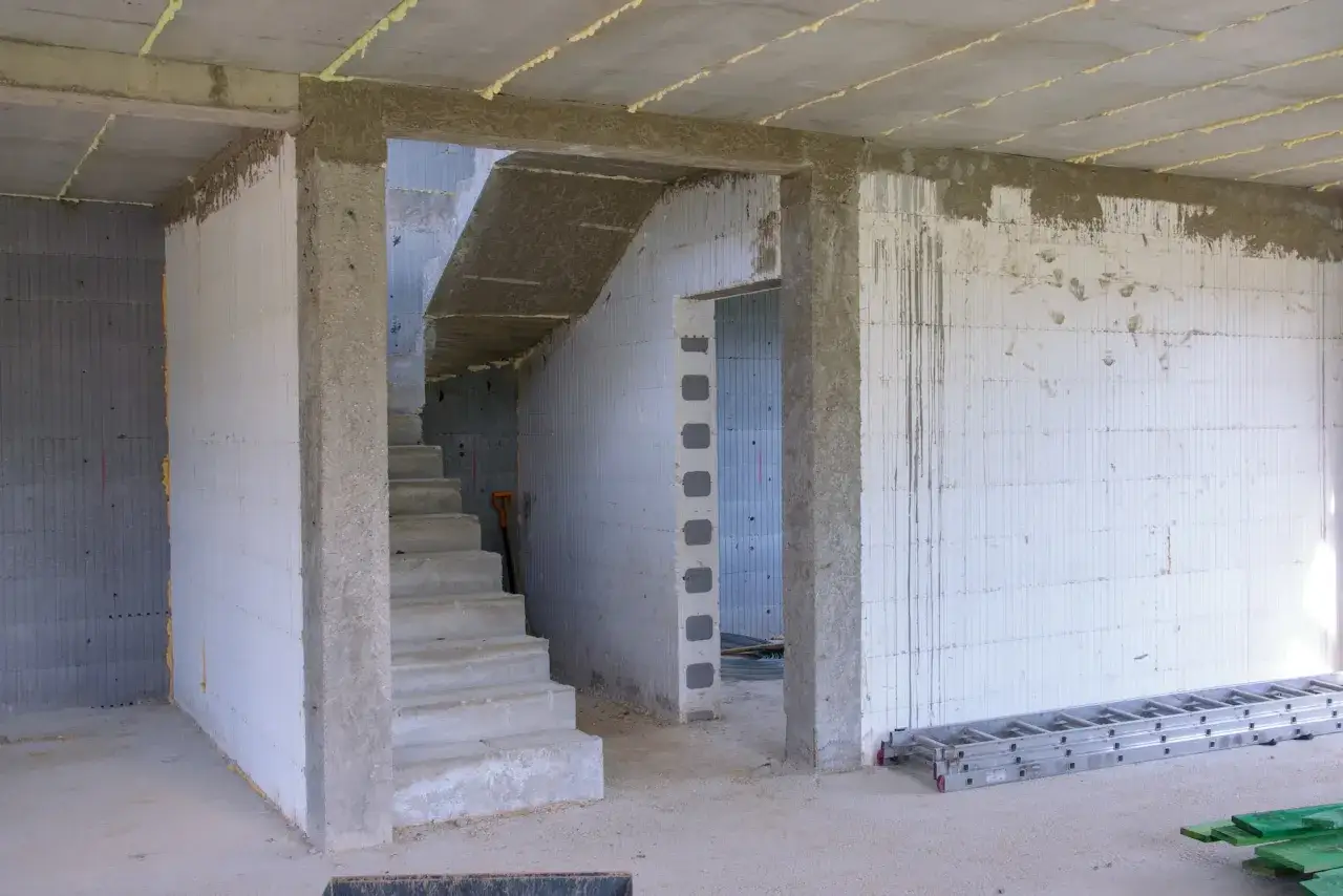 Wnętrze w budowie. Schody prowadzą do góry, obok otwór na drzwi 80. Ściany z białych pustaków, na podłodze beton.